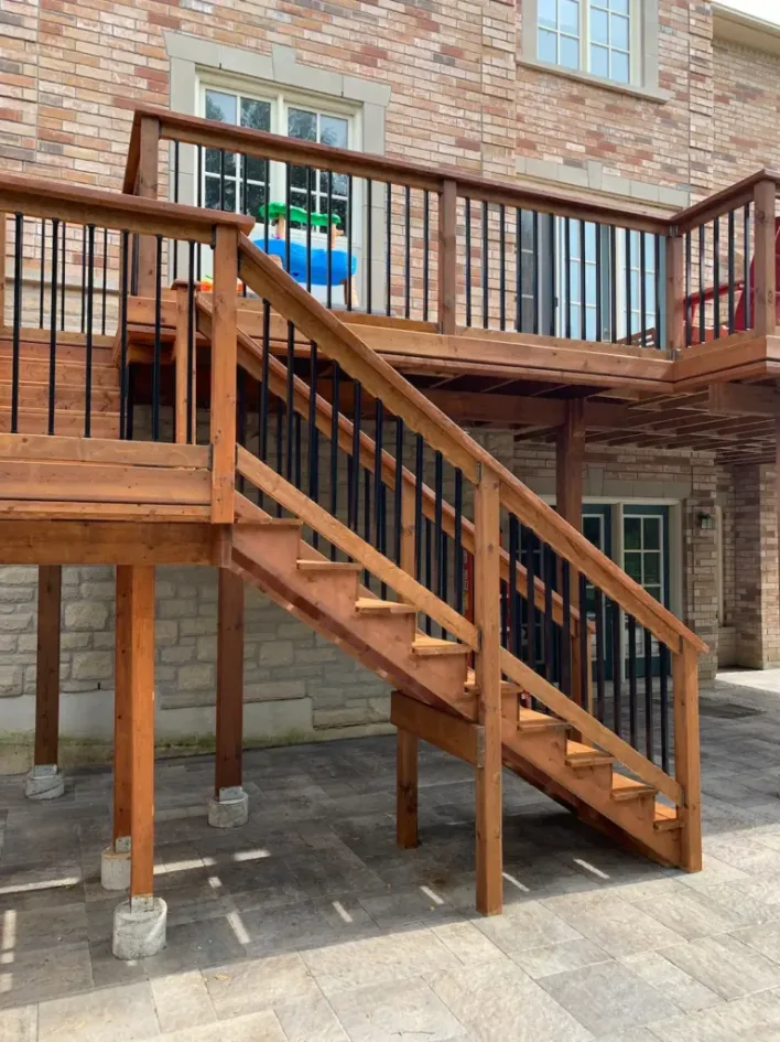 raised wood deck with stairs and black metal railings over interlocking patio