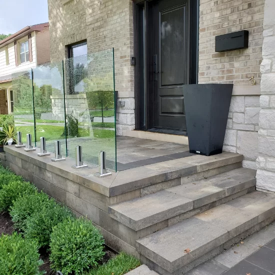 Front entrance with concrete steps, glass railing panels, and modern landscaping around the porch area, image by OAKS Home Services