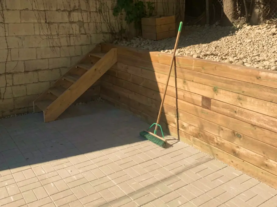 Gray interlocking stone patio with wooden retaining wall and landscaped slope, image by OAKS Home Services