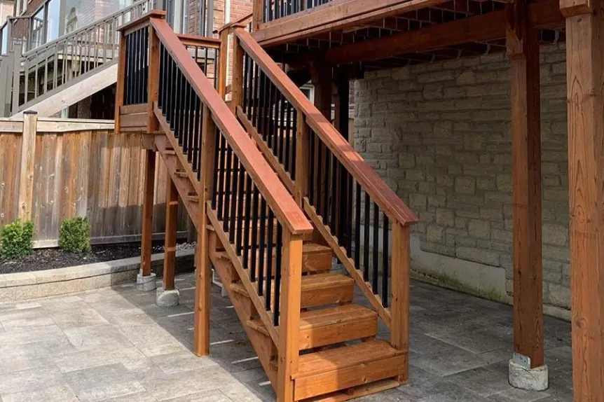 Wood deck stairs with black metal balusters and paved patio below