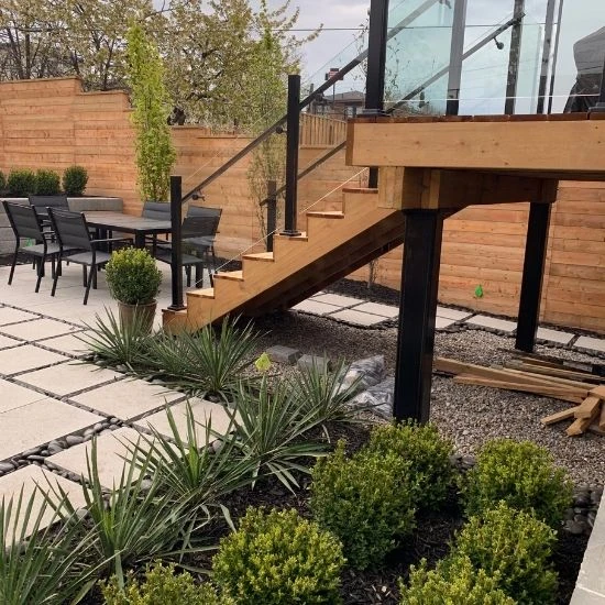 Backyard deck stairs with glass railing, patio seating, and structured planting design
