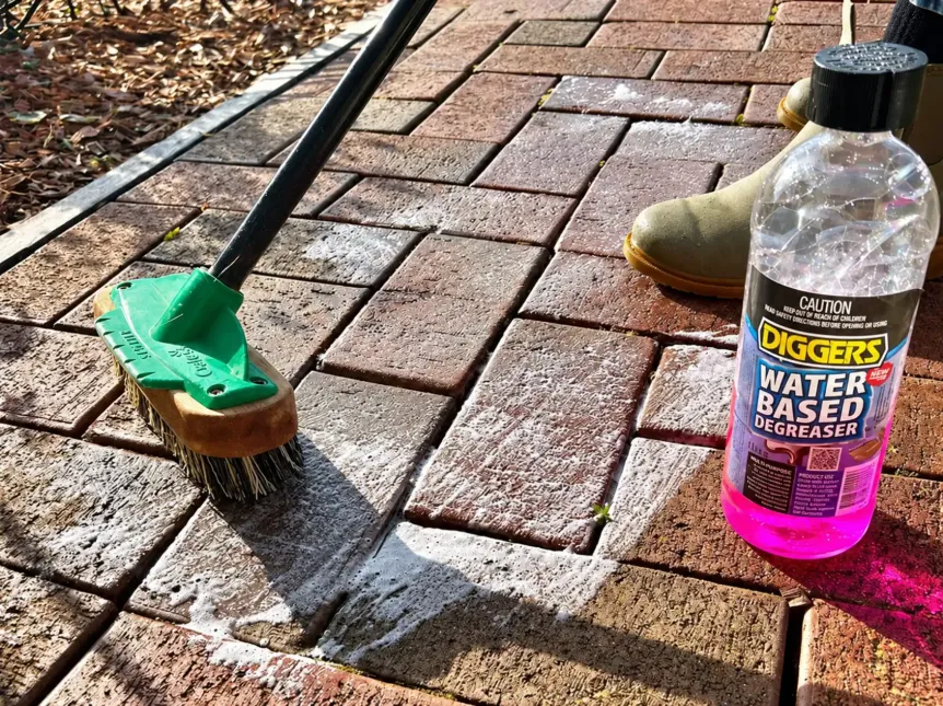 Cleaning brush and degreaser beside foamy brick pavers, photo Oakshs