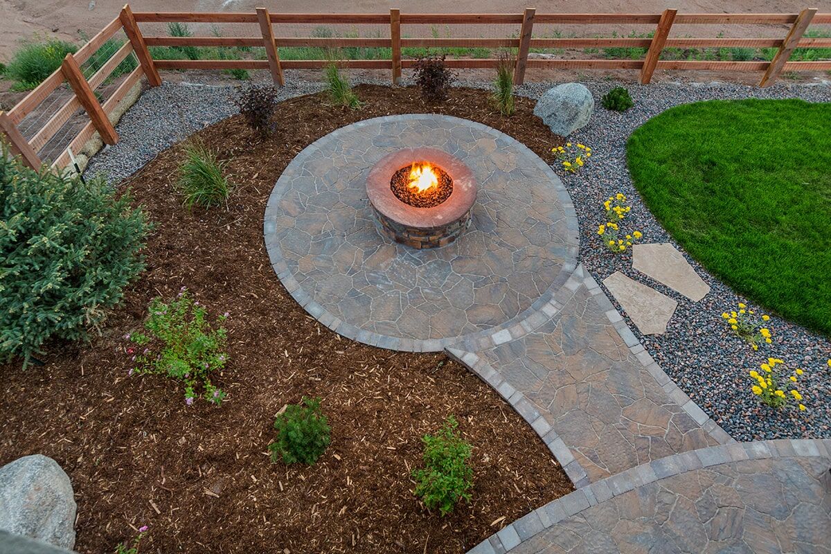 Stone fire pit patio with curved paver path and planting beds