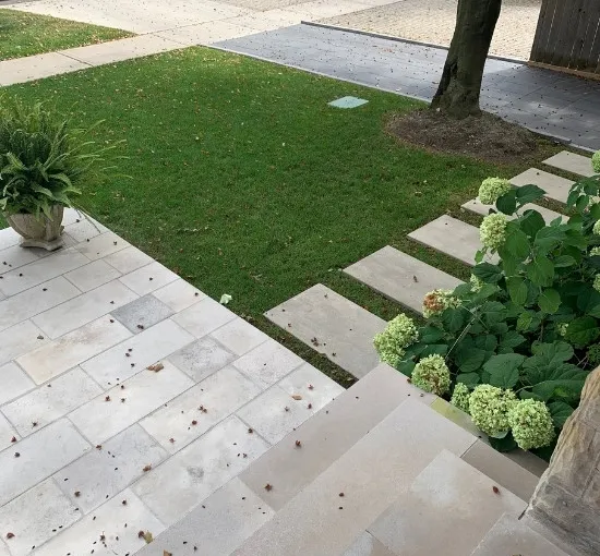 Clean stone steps and walkway leading to a green front lawn with planting beds and stepping stones