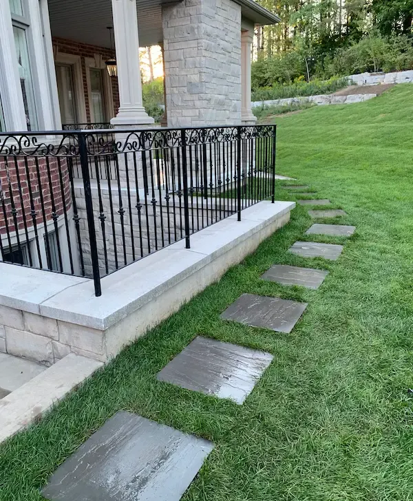 Stepping-stone walkway leading across lawn beside a raised porch railing