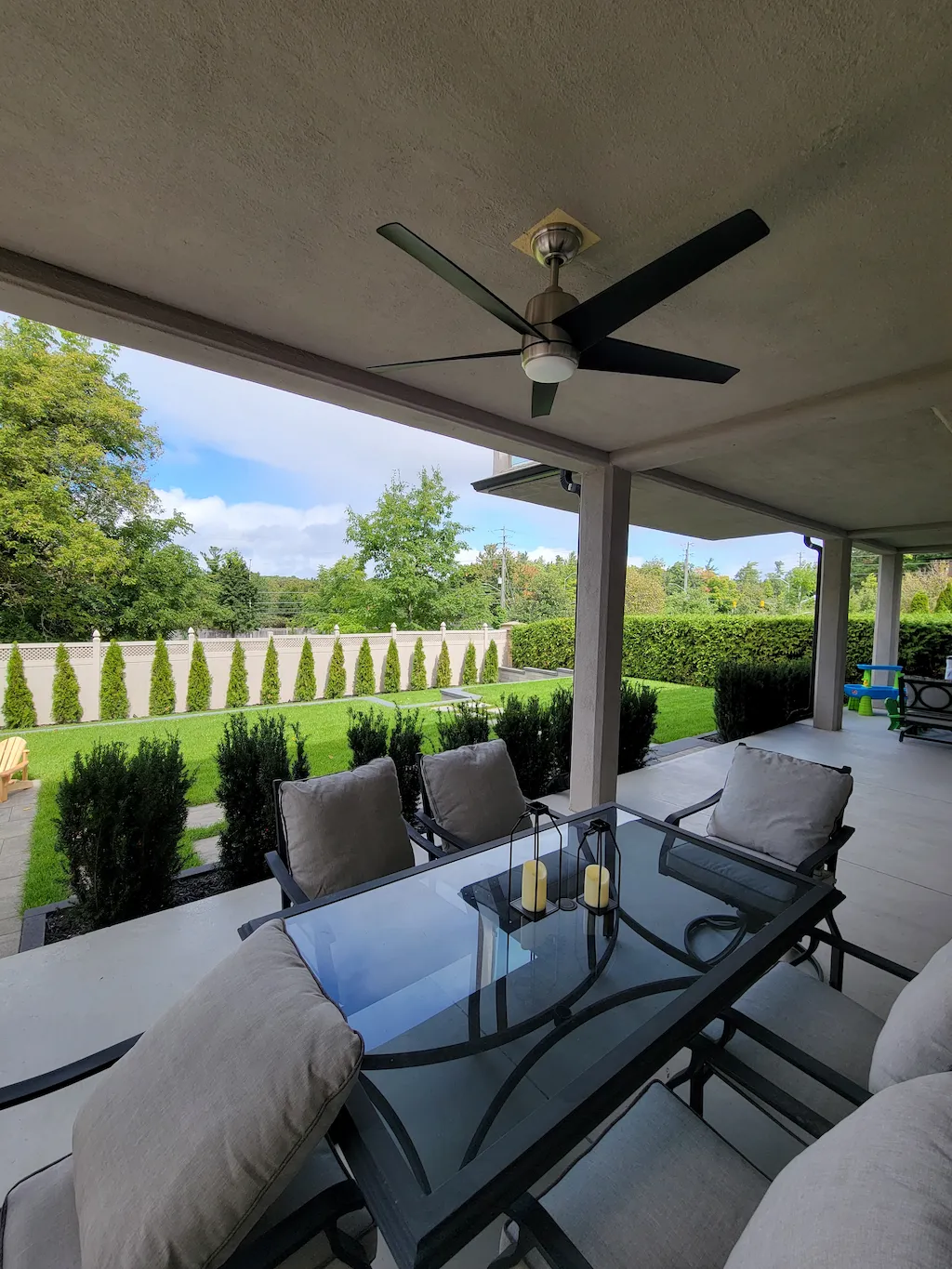 covered backyard patio dining area with ceiling fan, glass table and outdoor seating