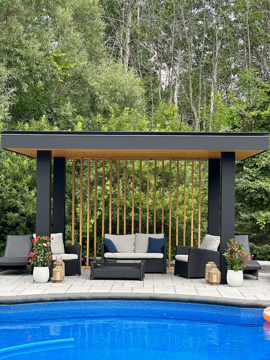 modern poolside pergola with wood slat wall, black posts and outdoor seating lounge