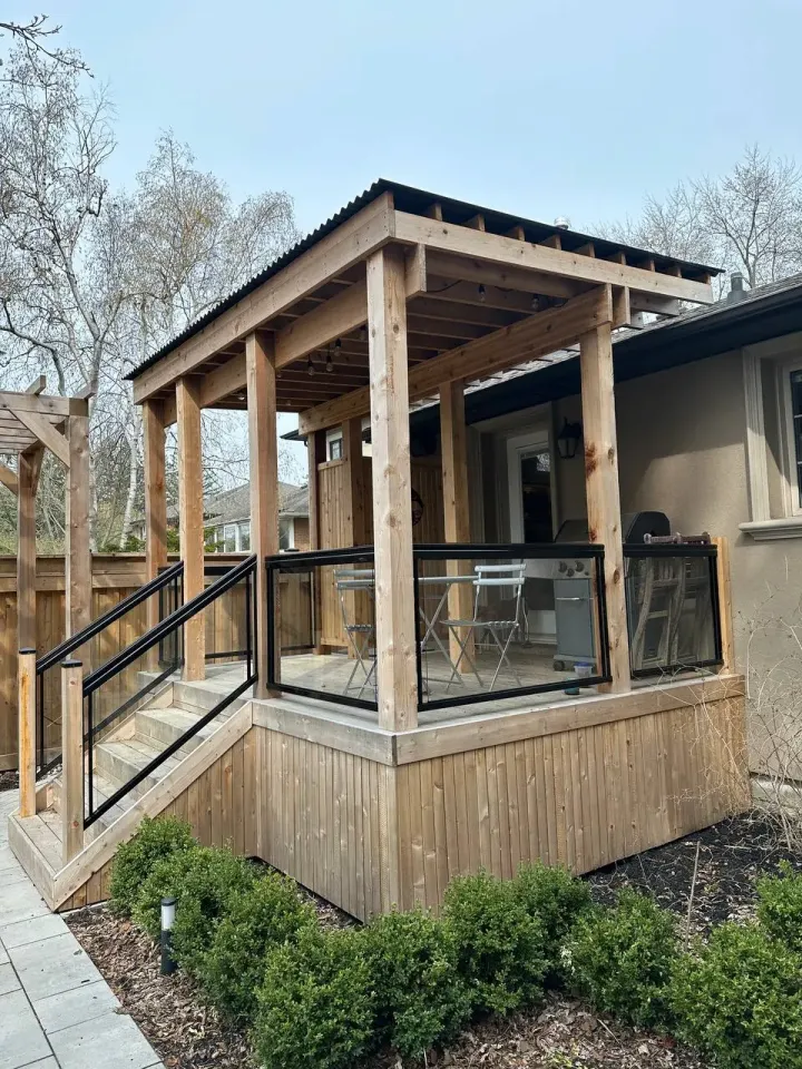 raised backyard deck with wood pergola cover, stairs and glass railing seating area