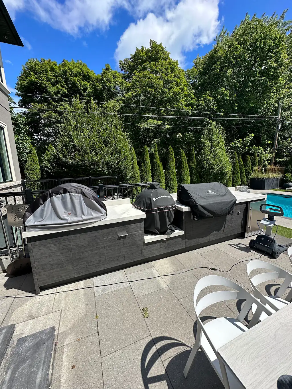 large outdoor kitchen with multiple grills, stone patio and poolside backyard setting