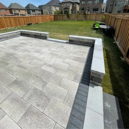 Backyard with interlocking stone patio, built-in seating walls, and wooden privacy fence surrounding the lawn, image by OAKS Home Services