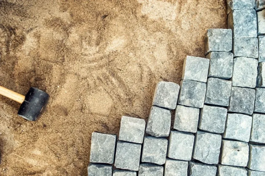 Close-up of interlocking stone pavers being installed on sand base with rubber mallet