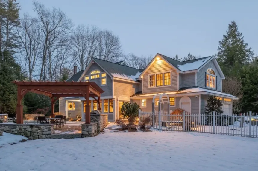 Two-story home with pergola and interlocking patio covered in snow at dusk