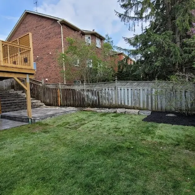 Backyard landscaping with sod lawn, interlocking patio area, and wooden deck, image by OAKS Home Services