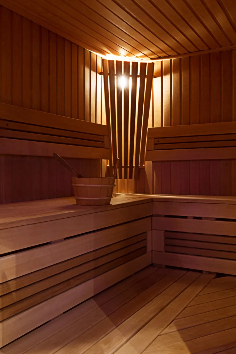 Cedar sauna interior with tiered benches, wooden bucket, and warm lighting, photo by Oaks