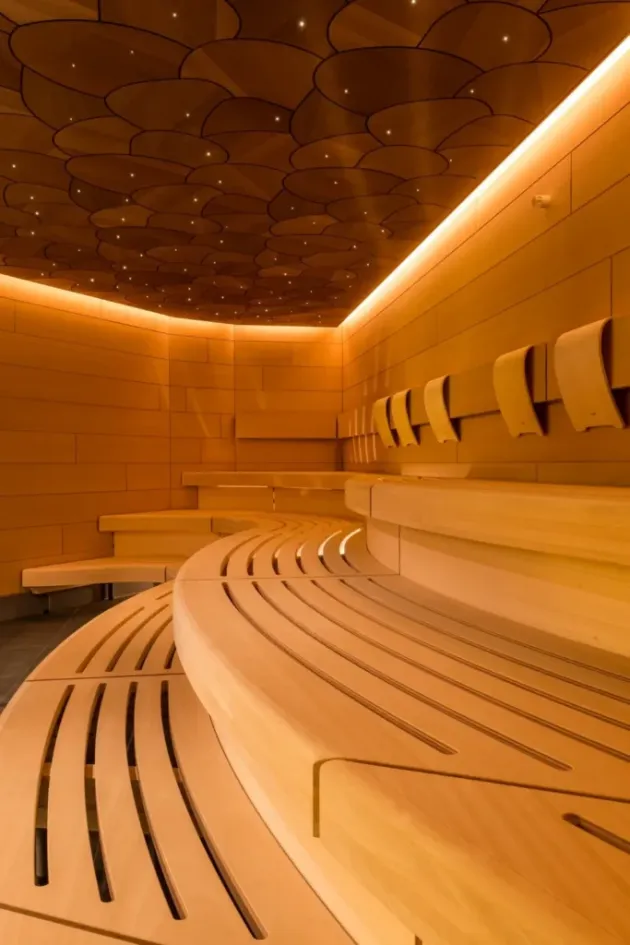 Custom sauna with curved wooden benches and integrated ceiling lighting, photo by Oaks