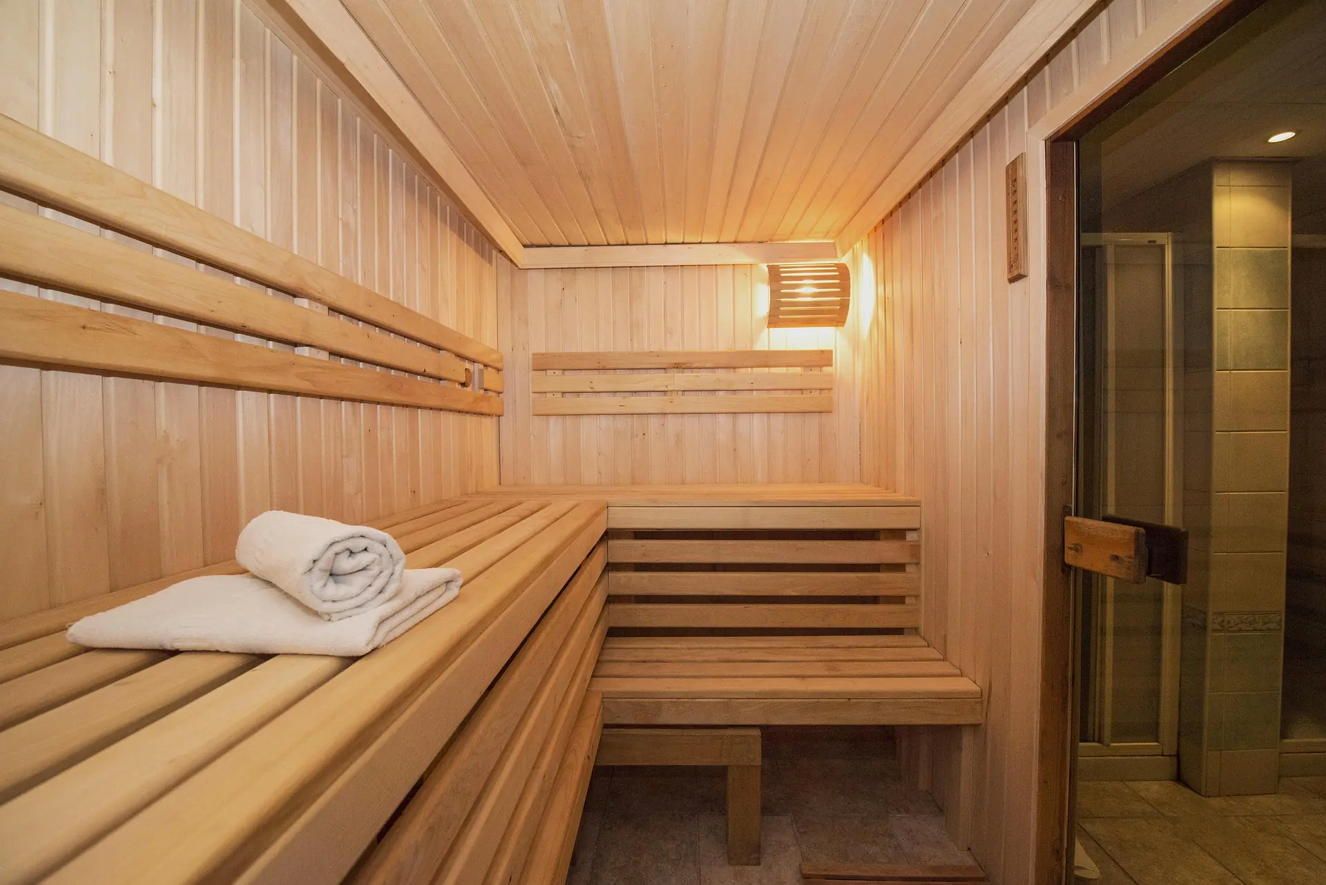 Light wood indoor sauna with L-shaped benches, towels, and a glass door, photo by Oaks