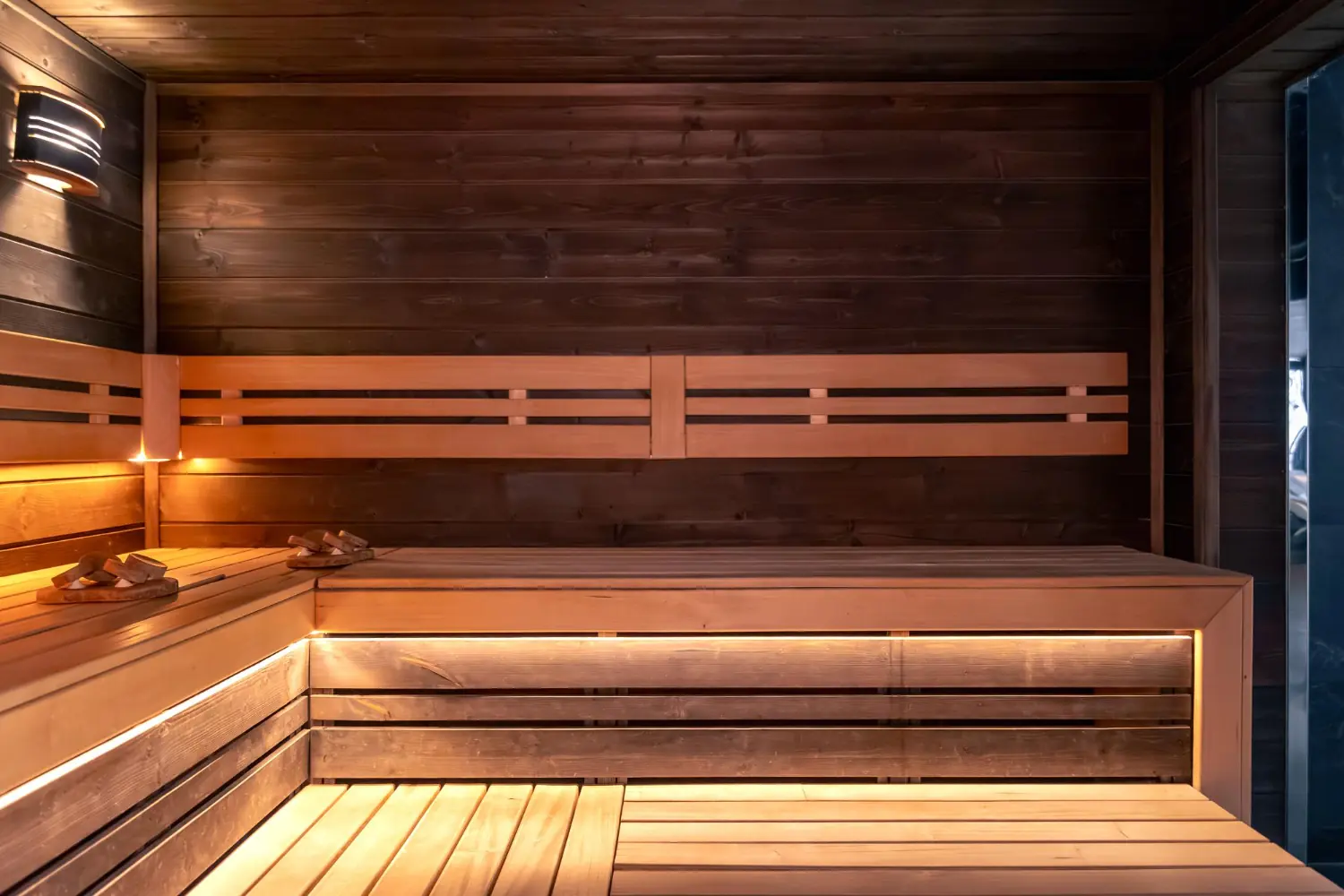 Custom sauna benches with concealed LED lighting and dark wood walls, photo by Oaks