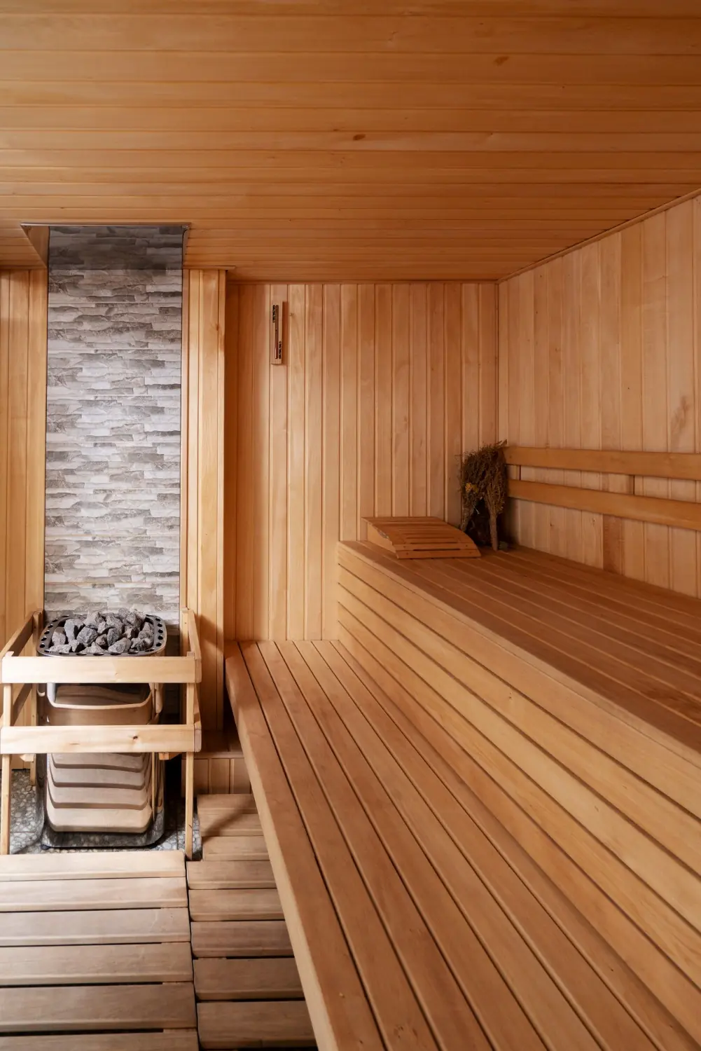Light wood sauna with an electric heater, stone accent wall, and tiered benches, photo by Oaks