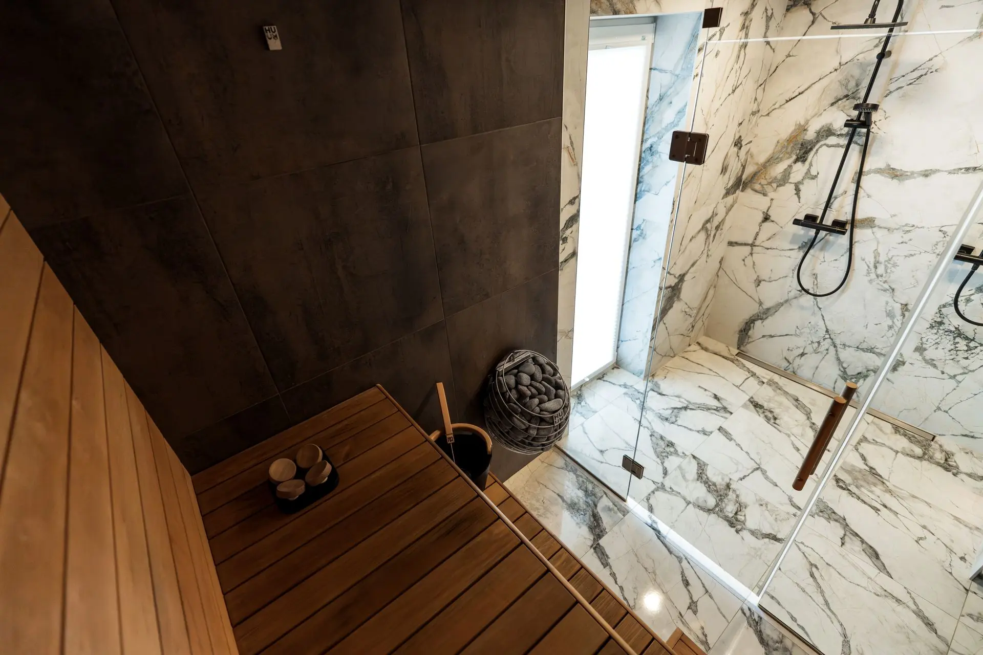 Home sauna with a stone heater beside a glass-enclosed shower, photo by Oaks