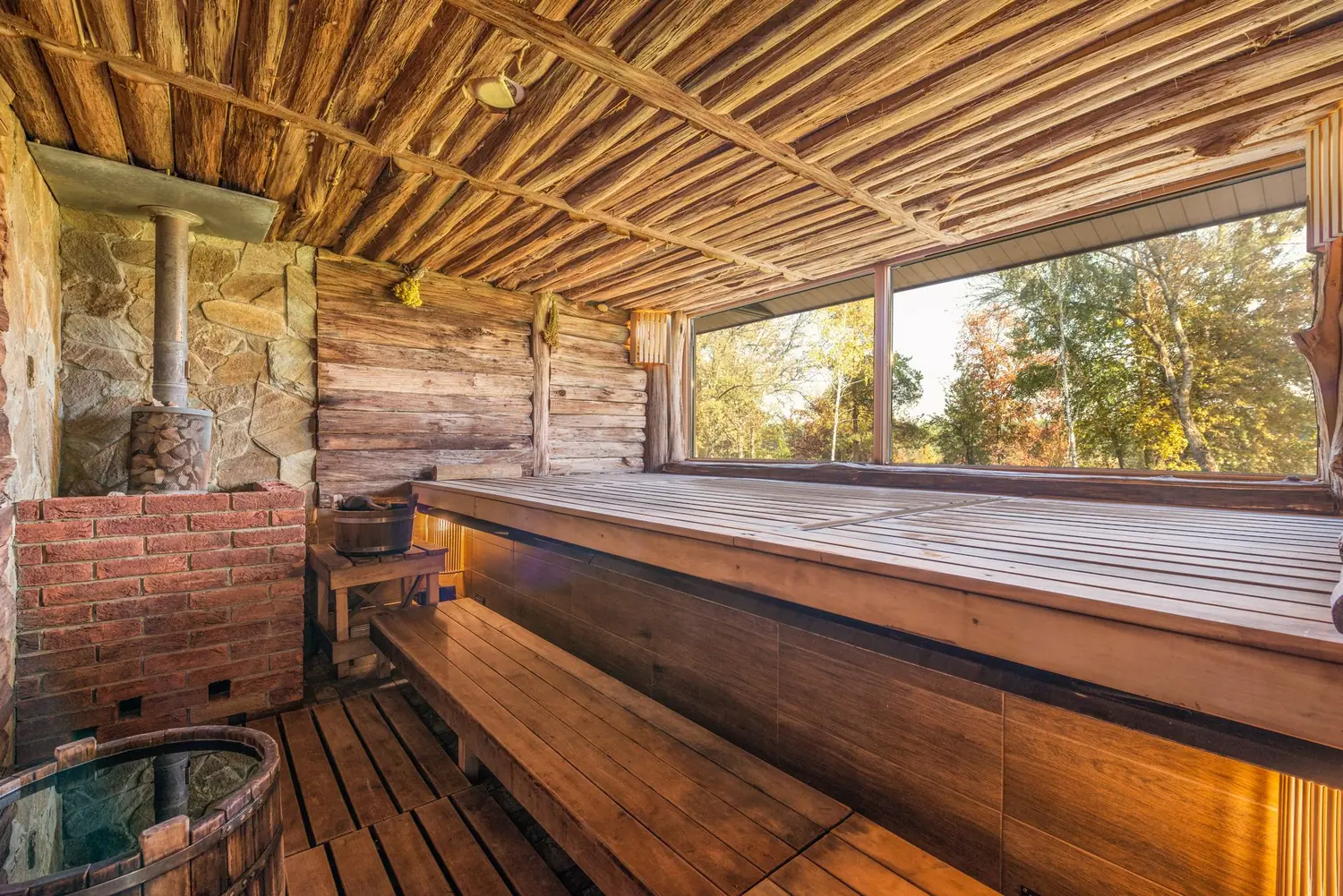 Rustic wood-burning sauna with tiered benches and large windows, photo by Oaks