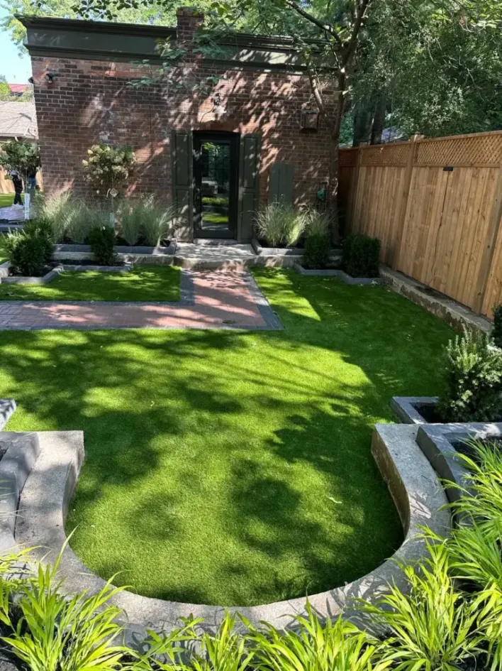 backyard landscape design with green lawn, stone edging, garden beds and brick pathway leading to house