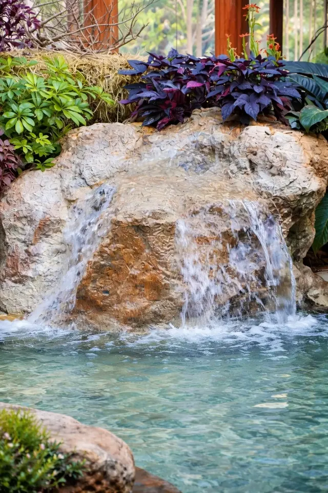 natural stone waterfall flowing into backyard pond surrounded by lush plants and landscaping
