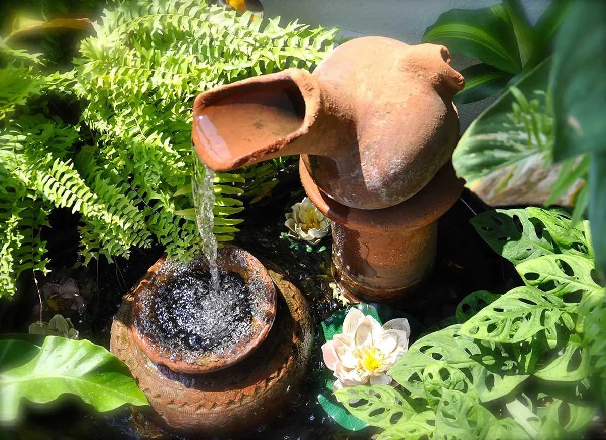 decorative ceramic jar water feature with flowing water surrounded by tropical plants and pond flowers