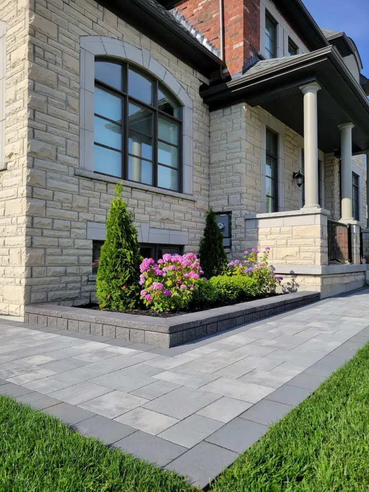 interlocking paver walkway with raised garden bed and flowers in front of stone house