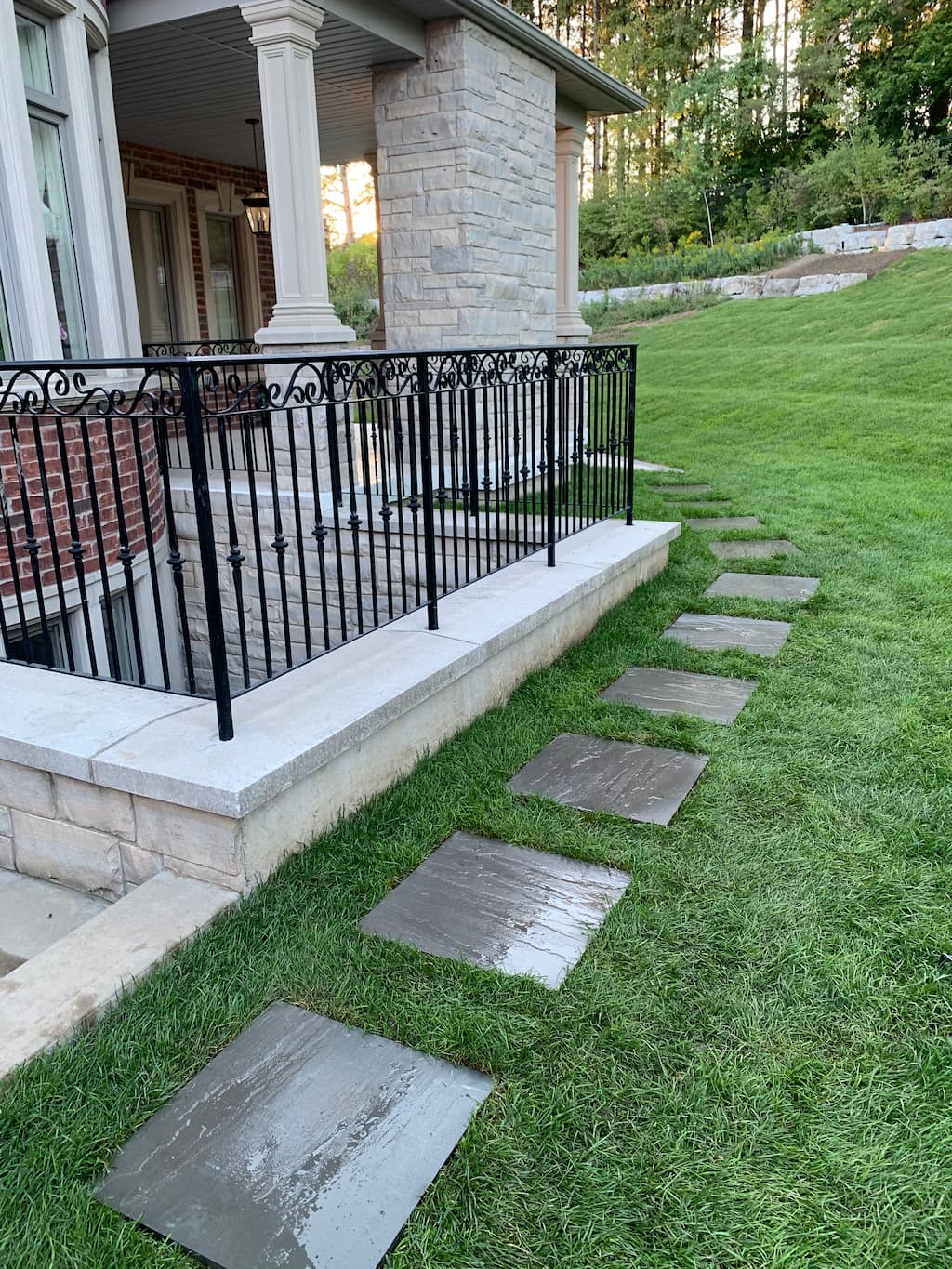 backyard landscaping with stepping stone path through green lawn, stone patio edge, and modern house exterior
