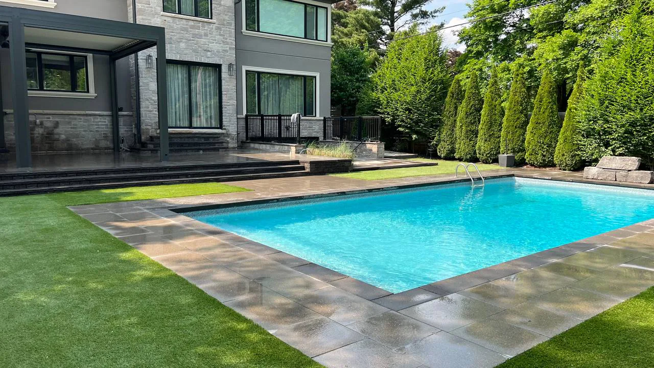 luxury backyard with rectangular pool, stone patio, modern house, and landscaped greenery with privacy trees