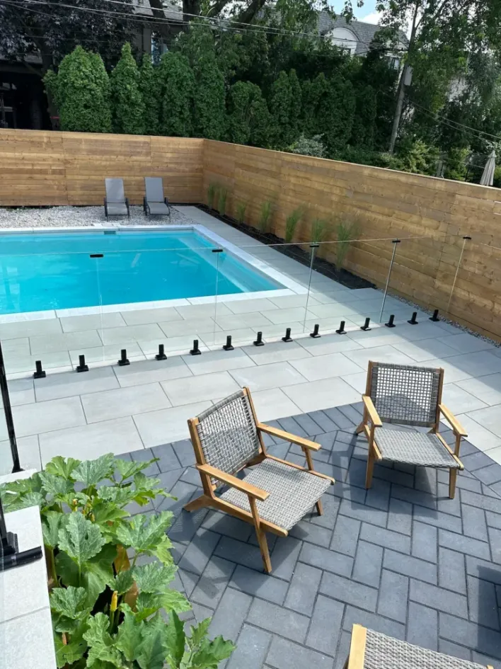 modern backyard landscaping with swimming pool, glass fence, stone patio, wood privacy fence, and outdoor seating area