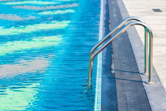 swimming pool with metal ladder, clear blue water, and clean straight pool edge with modern deck surface