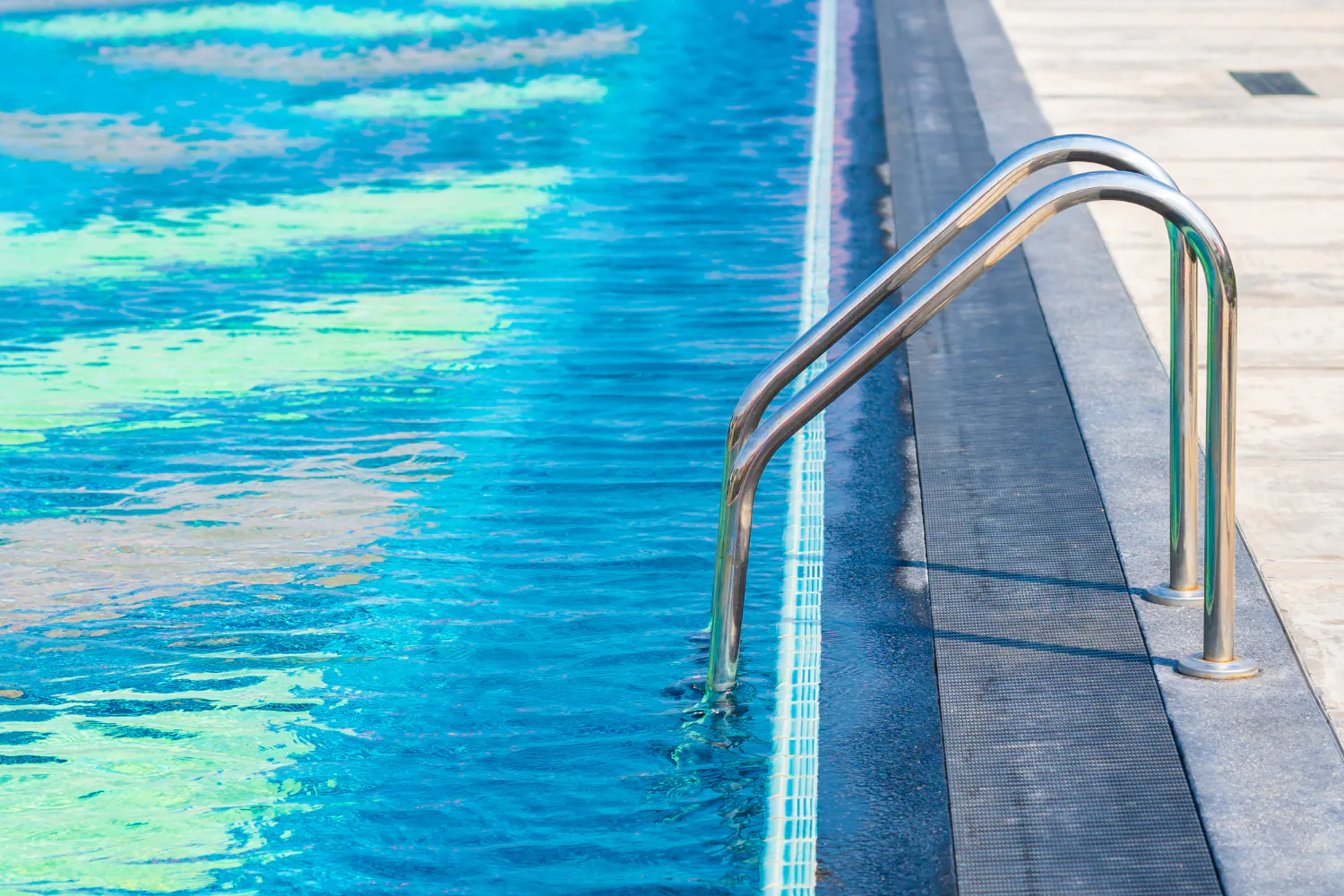 swimming pool with metal ladder, clear blue water, and clean straight pool edge with modern deck surface