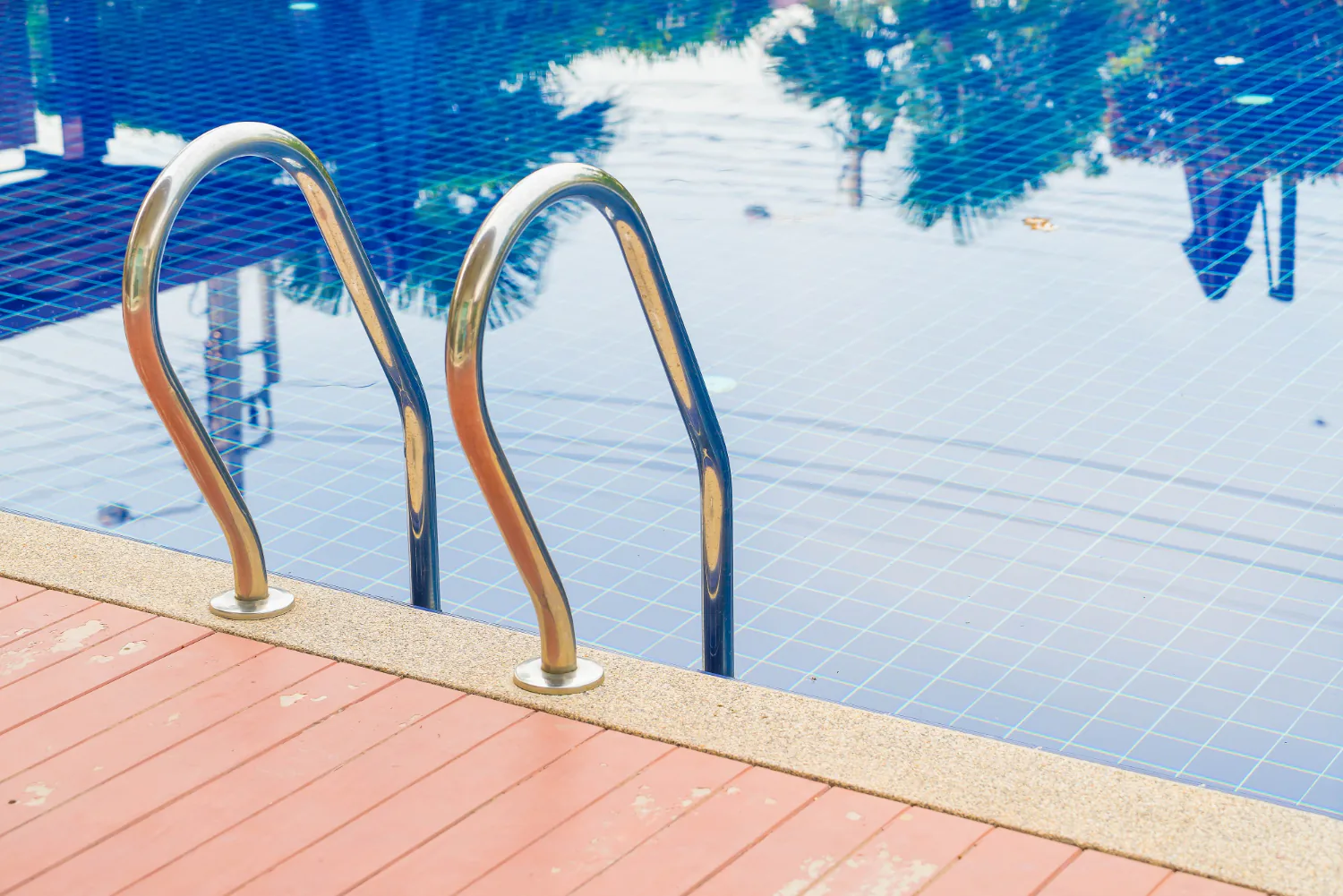 swimming pool with metal ladder, blue tiled water, and textured deck surface in bright daylight