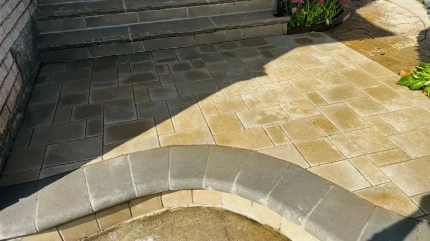 Interlocking paver patio with warm-toned stones, curved seating wall, and steps leading to backyard entrance