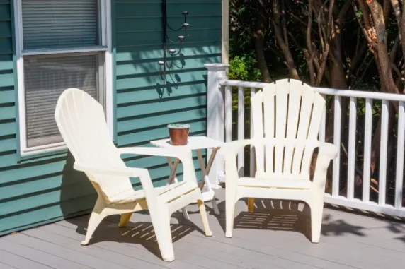 Two white Adirondack chairs on porch deck with small side table