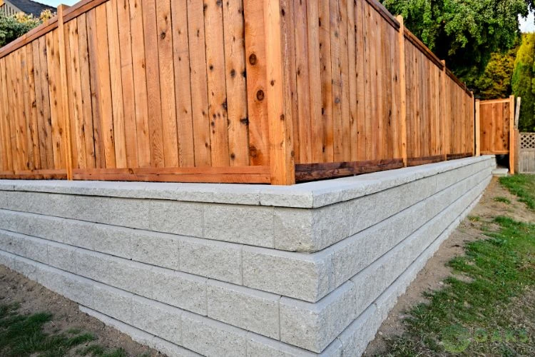 Concrete block retaining wall supporting wooden privacy fence in backyard
