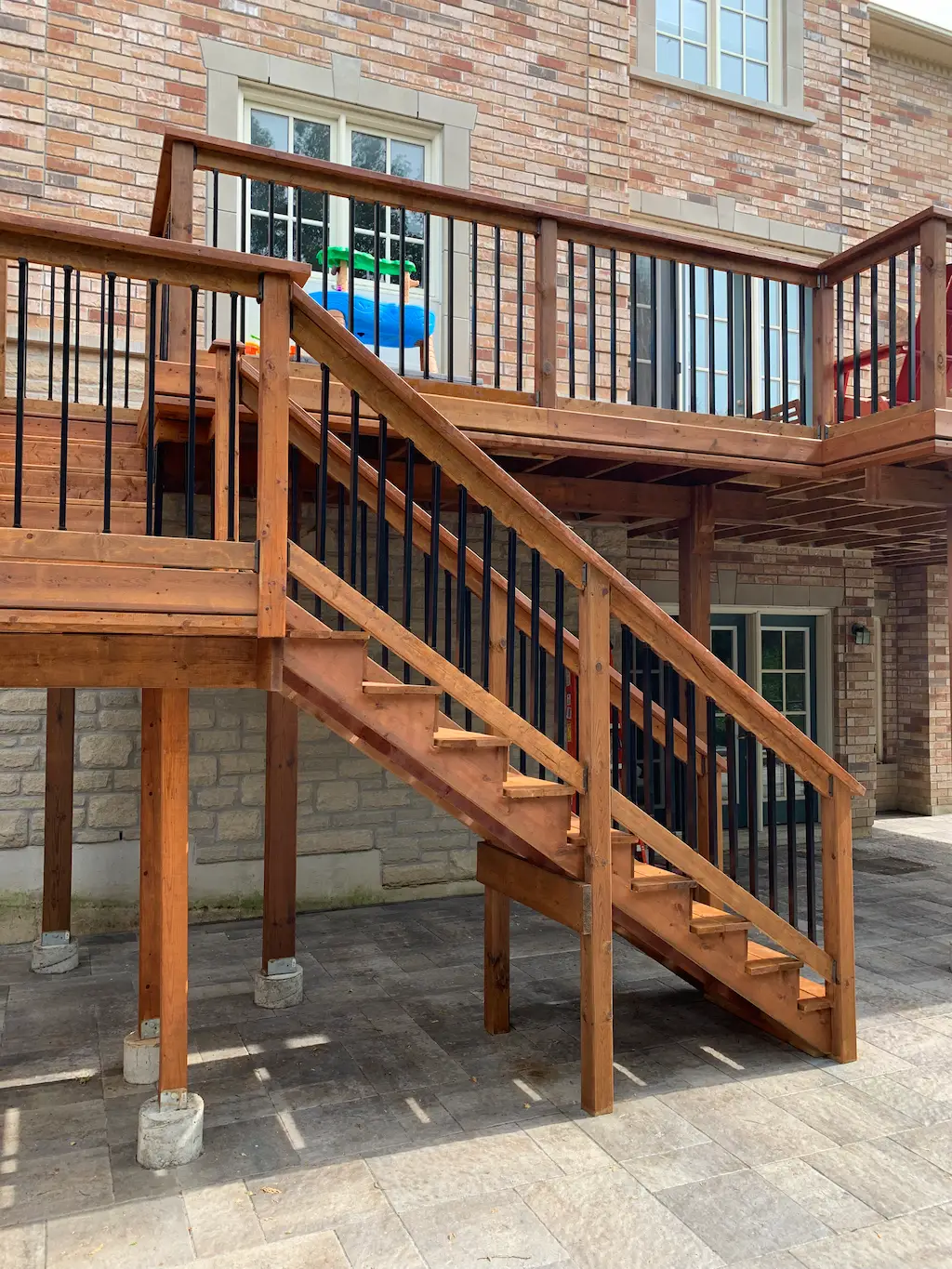 raised wood deck with stairs and black metal railings over interlocking patio