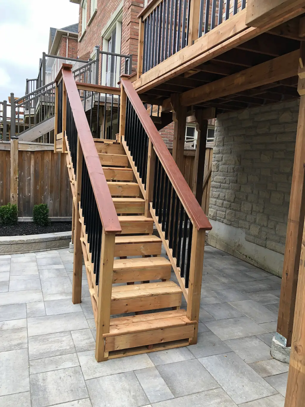 wood deck stairs with black metal balusters leading to raised backyard deck