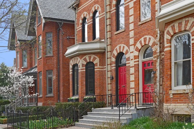 Historic Toronto brick homes with decorative fencing and red front doors along a residential street