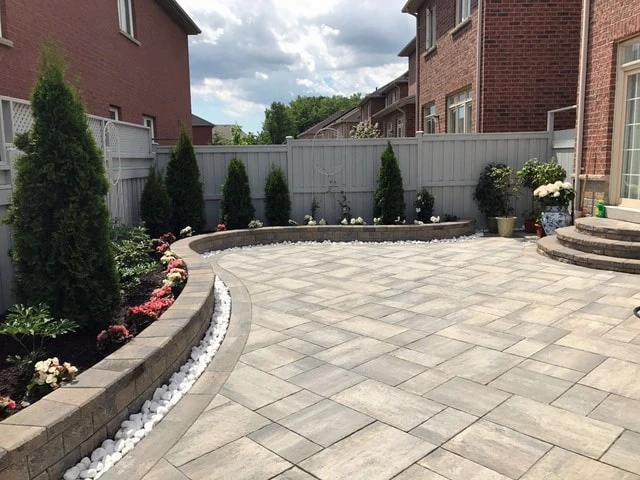 Spacious interlocking patio with curved retaining wall and decorative planting beds
