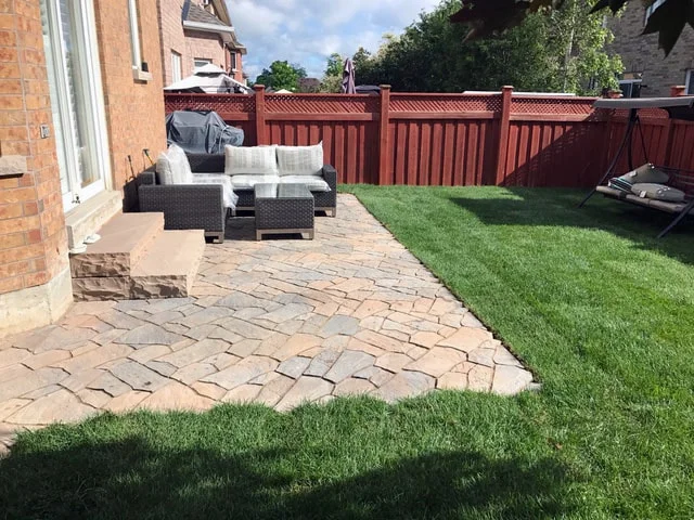 Natural stone patio with outdoor seating beside green lawn and privacy fence
