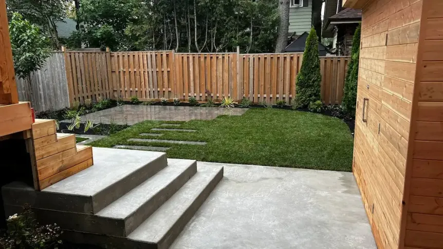 Modern backyard with concrete steps, lawn, and minimalist planting along wood fence