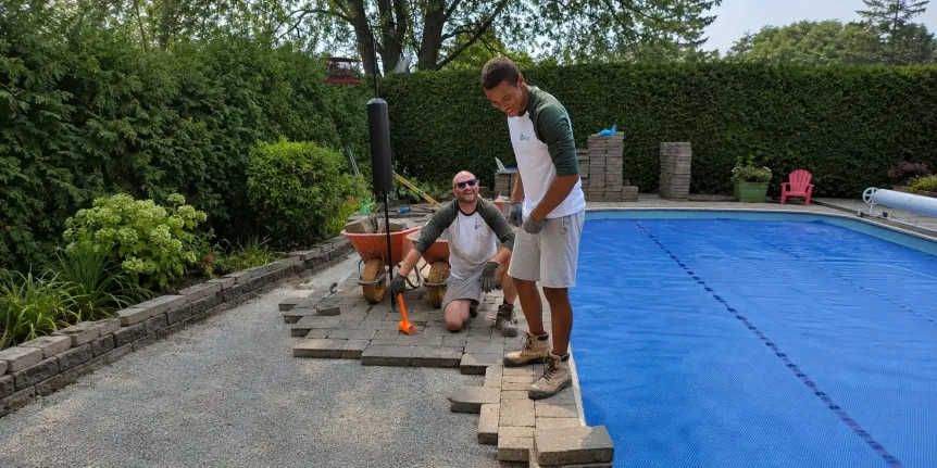 Landscaping crew installing interlocking pavers around a backyard swimming pool patio, image by Oaks