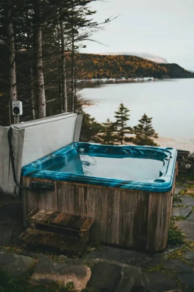 Backyard hot tub with open cover and blue shell overlooking coastal water, photo by oakshs.ca