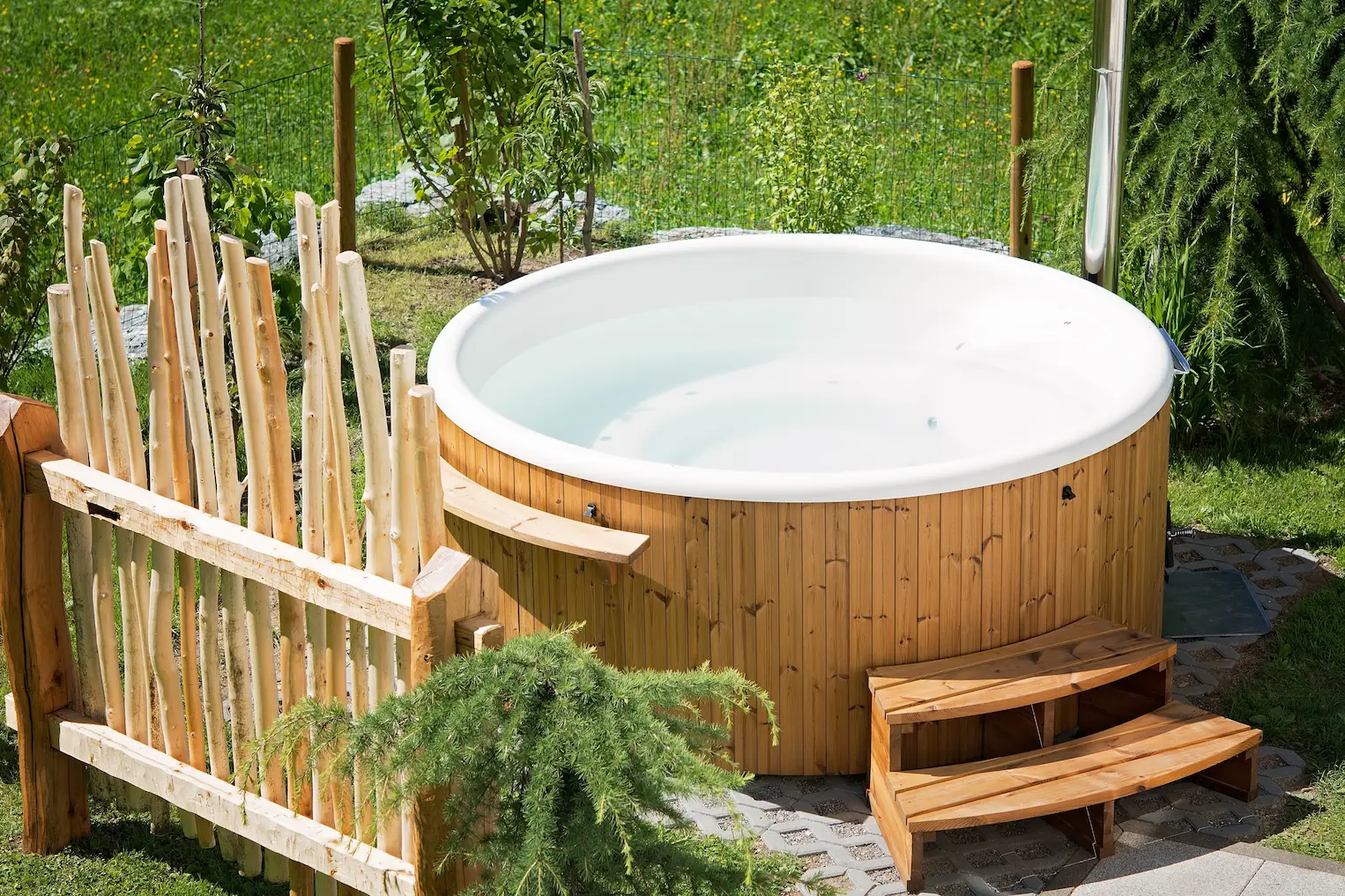 Round hot tub with wood cabinet and steps in a sunny garden, photo by oakshs.ca