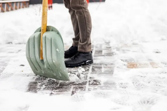 Person clearing snow from interlocking driveway with shovel during Canadian winter