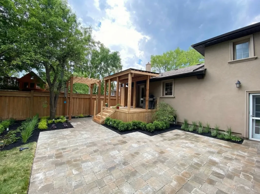 backyard interlocking patio with wood deck pergola garden beds and landscaped yard