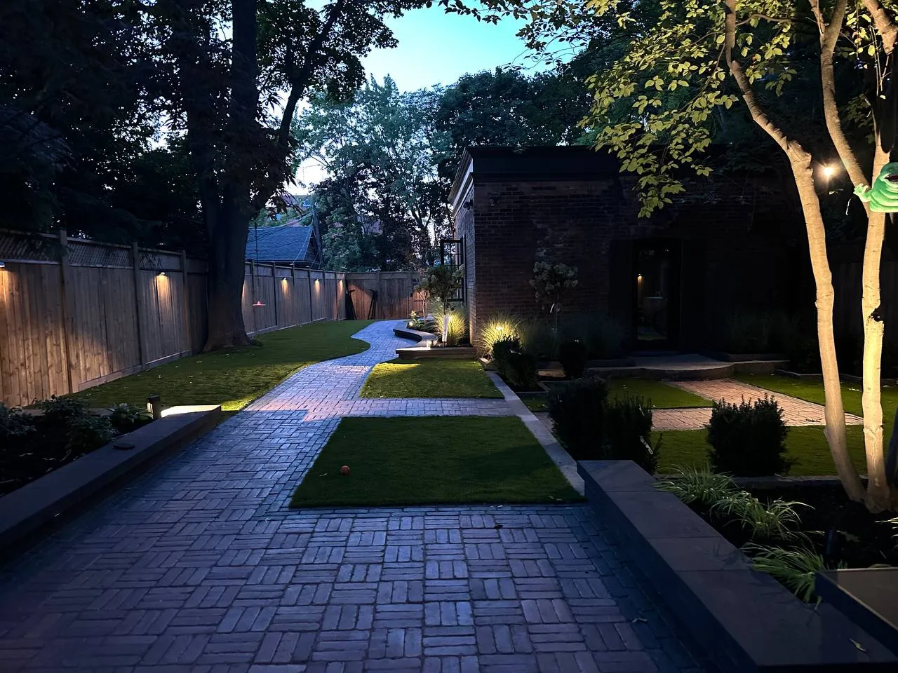 backyard landscape lighting with illuminated pathway, trees and modern garden design at night