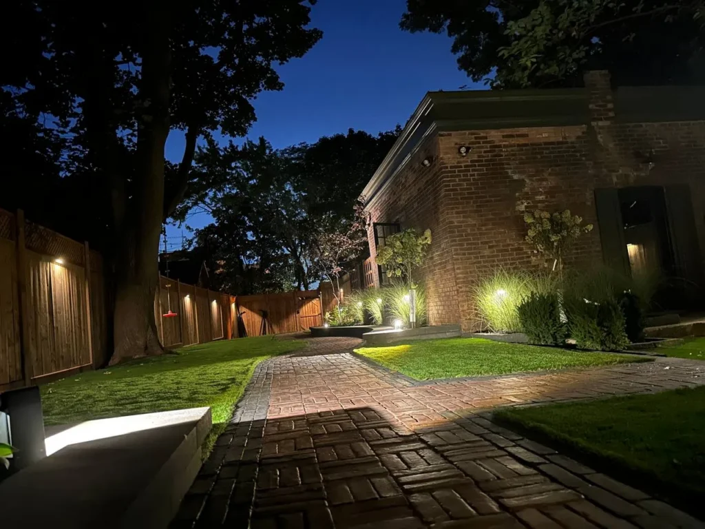 backyard walkway with landscape lighting, brick path and illuminated lawn at night